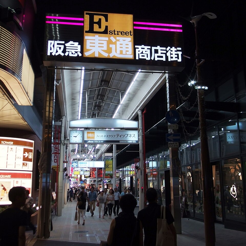 People walking beneath the illuminated Hankyu Higashidori shopping street entrance at night