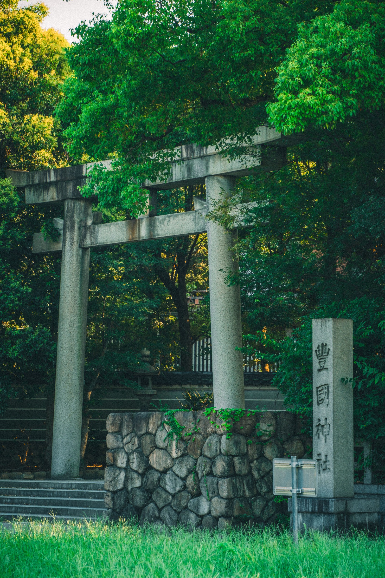 A stone torii surrounded by green trees at Hokoku Shrine