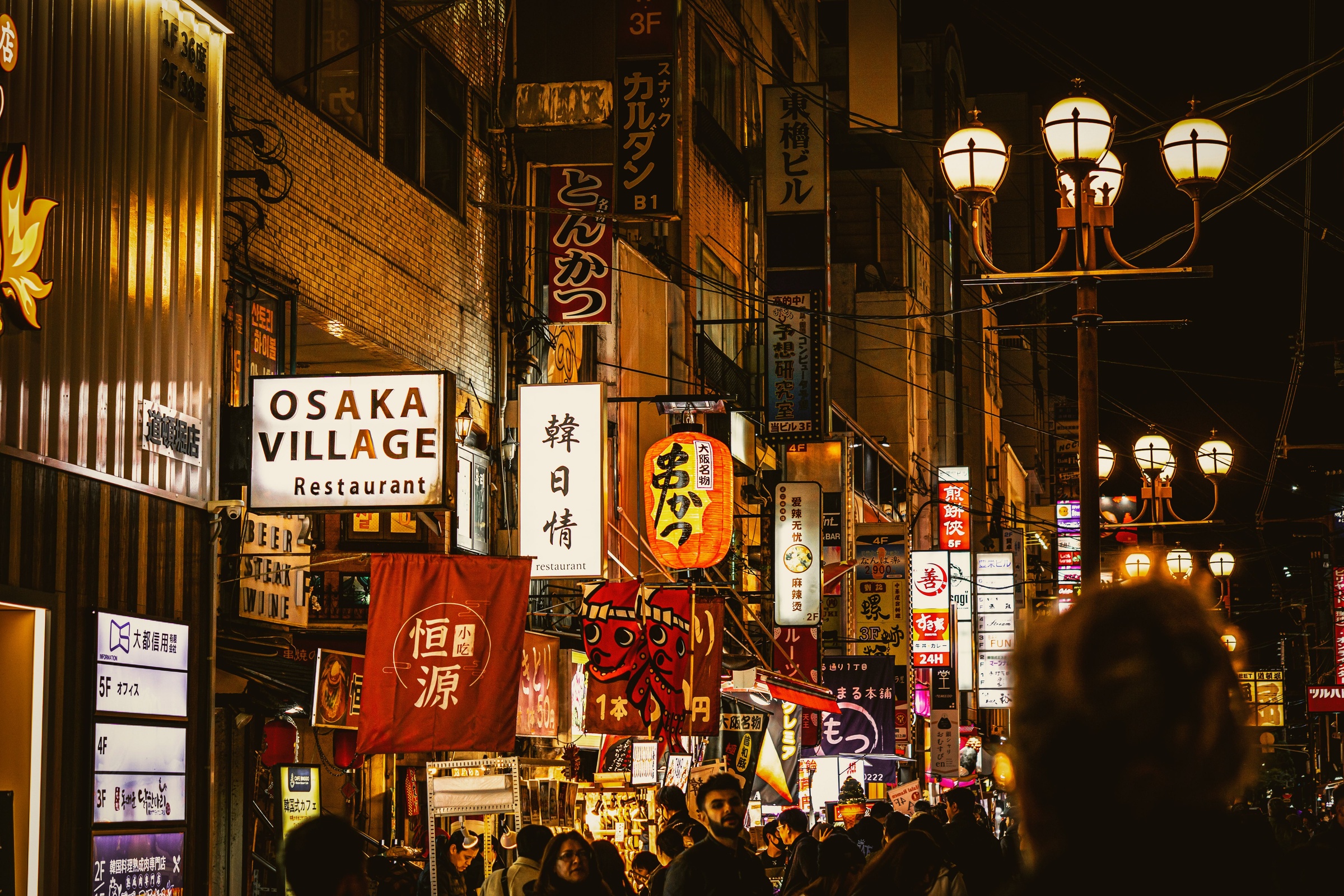 Warmly lit restaurant signs and visitors in the Dotonbori area