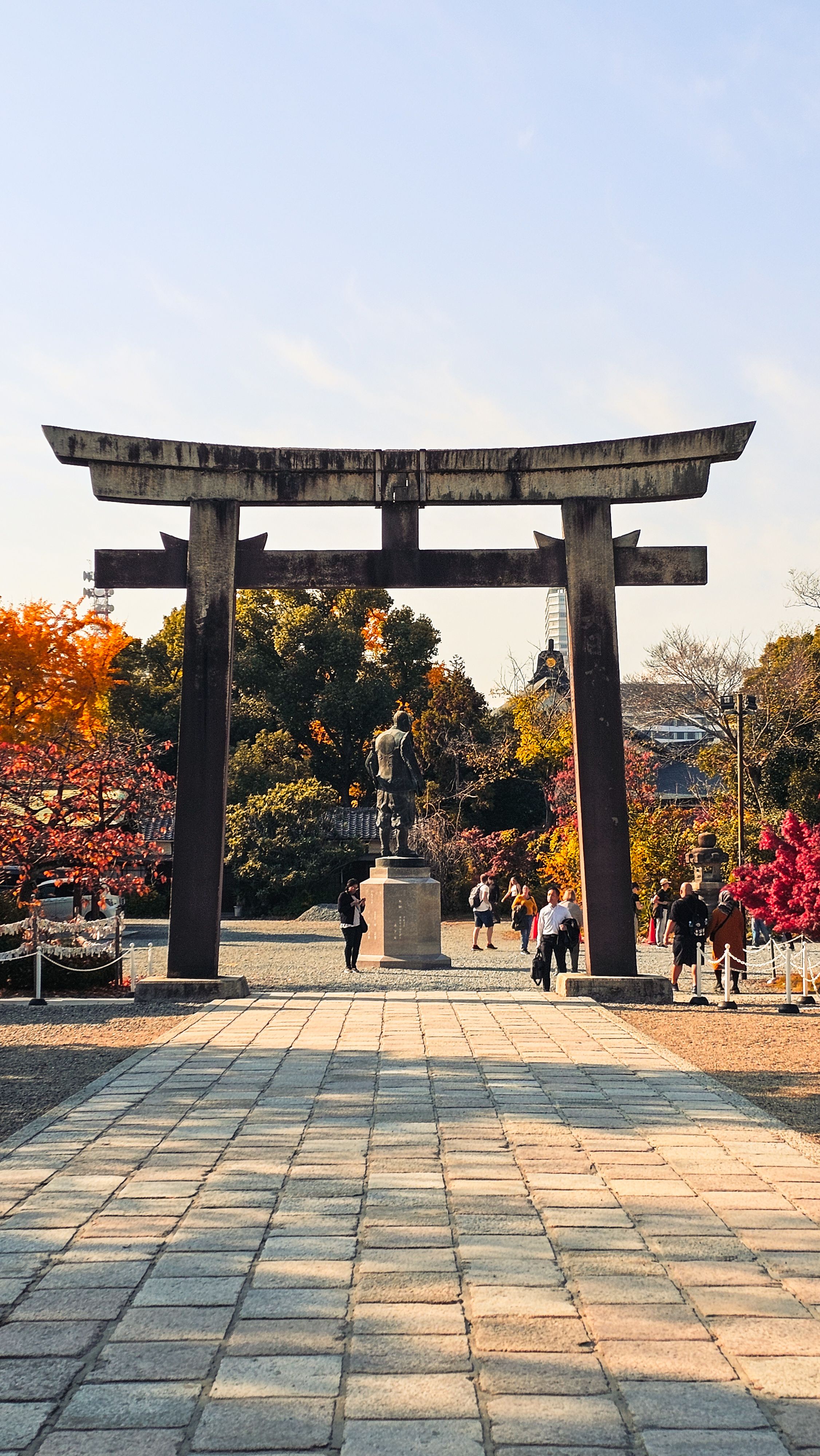Visitors beneath the stone torii at Hokoku Shrine with autumn leaves and the Hideyoshi statue