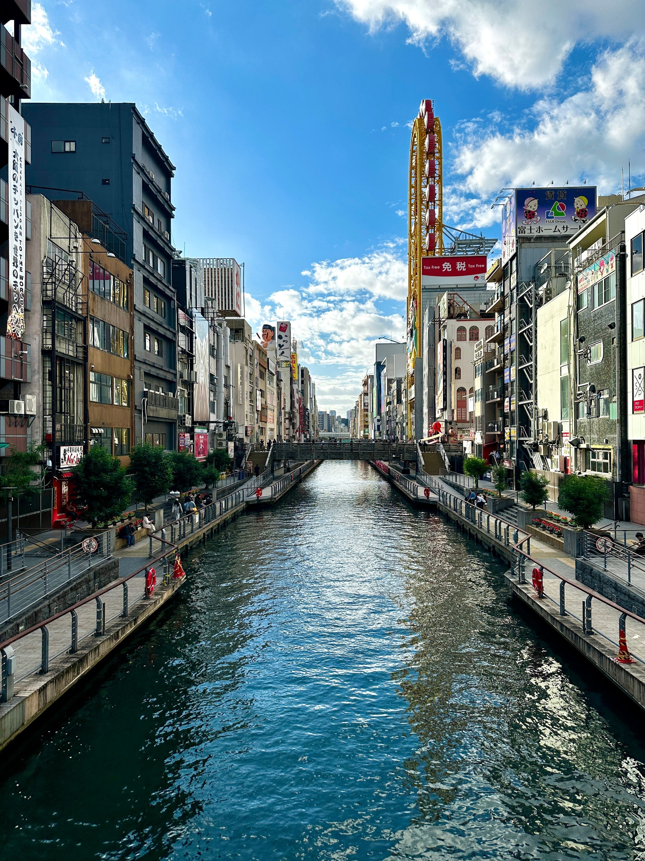 Restaurants and signs lining the Dotonbori canal beneath a blue sky