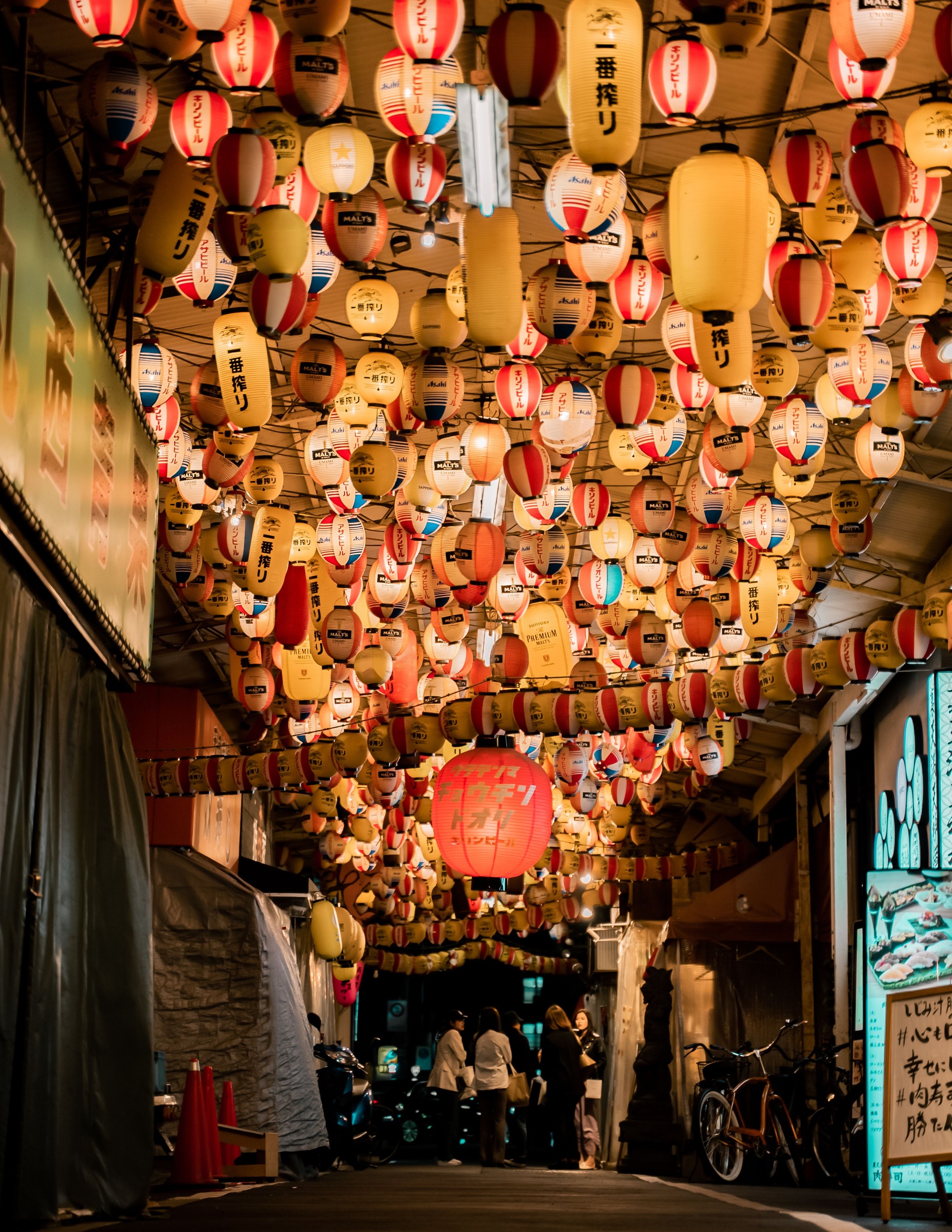 Rows of glowing lanterns above a narrow dining lane in Tenma