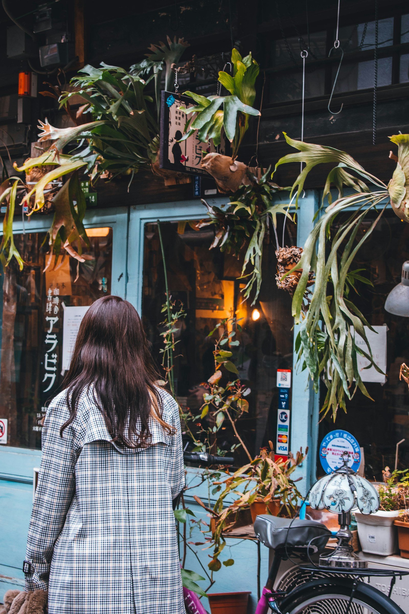 A visitor outside a Nakazakicho shop decorated with hanging plants and a turquoise window