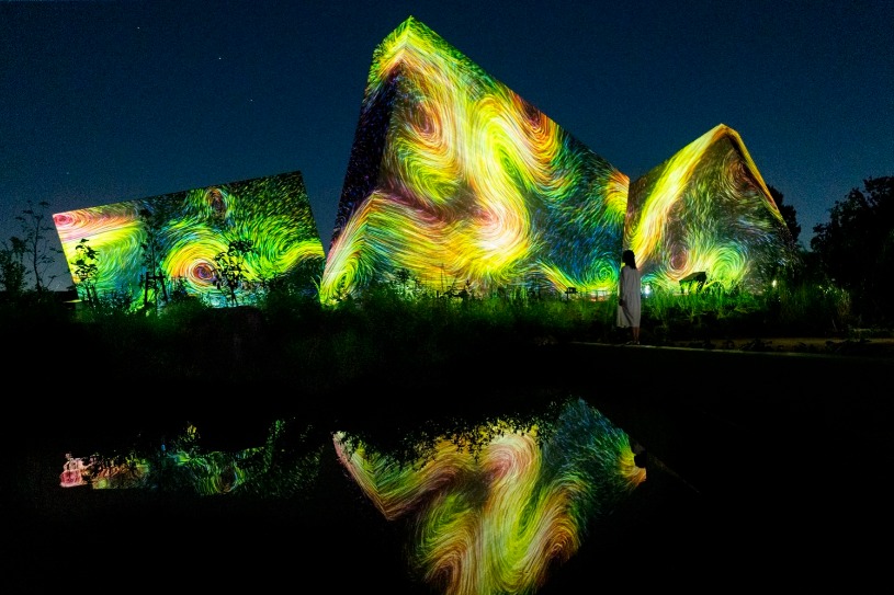 Colorful illuminated forms reflected in the water at teamLab Botanical Garden Osaka